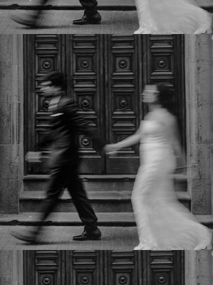 An artistic motion-blur photo in black and white, capturing the dynamic movement of the couple walking past a historic doorway.