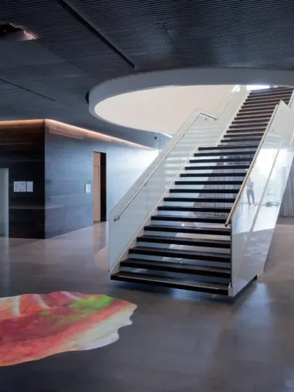 The main hall of the Virchow 16 building, showing the relationship between the sculptural white staircase and the colorful art projection on the floor. The space is defined by the interplay of form, color, and light.