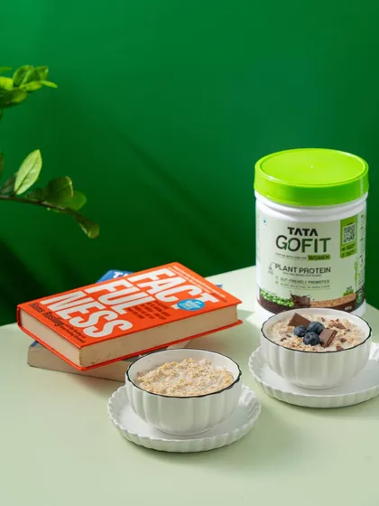 Showing the product as part of a healthy morning routine. Tata GoFit protein is presented alongside bowls of oats and a book, creating an aspirational breakfast scene.