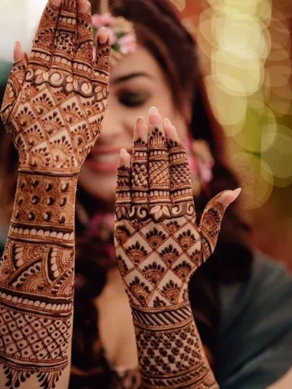 A beautiful shot of a bride showing off her intricate mehendi. The design is a classic grid and checkerboard pattern, known as jaali work, which looks stunning both up close and from a distance.