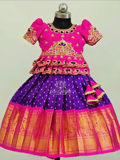 A vibrant pink and purple Pattu Pavadai. The blouse has a tiered peplum design and is detailed with rich gold embroidery, matching the wide zari border on the skirt.