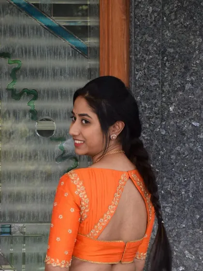 A client showing off the back of her custom orange blouse, which features a stylish cut-out design and delicate floral embroidery.