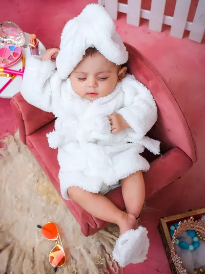 A fun and creative "spa day" theme for a baby. This shot shows the baby relaxing in a miniature chair, wrapped in a fluffy white robe.