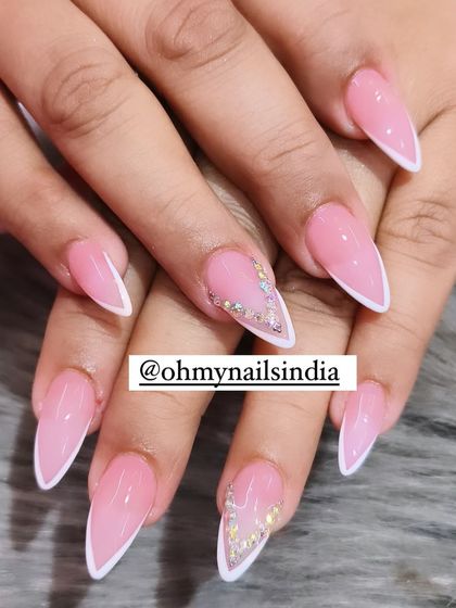 A chic twist on the classic French. This design features a soft pink base with a sharp, v-shaped white tip, accented with delicate crystal work for a touch of sparkle.