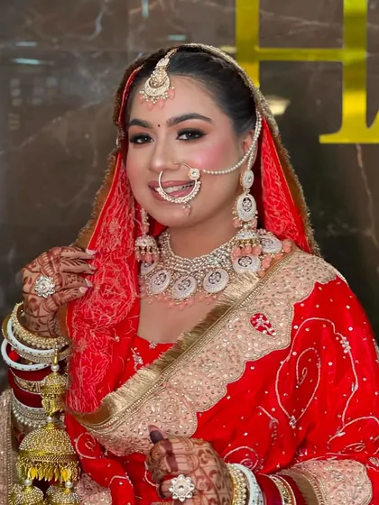 This bride looks stunning in her red and gold outfit. Her makeup features a soft pink blush and highlighter that catches the light beautifully.