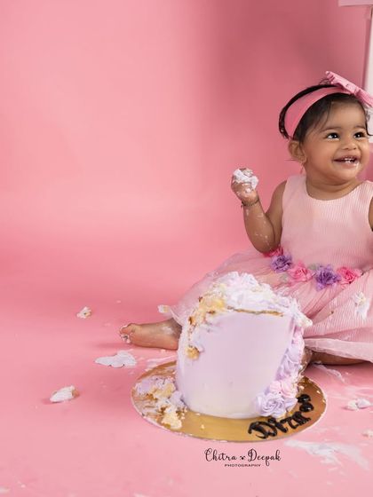 A happy baby girl enjoying her first taste of cake during her pink and purple themed cakesmash photoshoot in our Bangalore studio.
