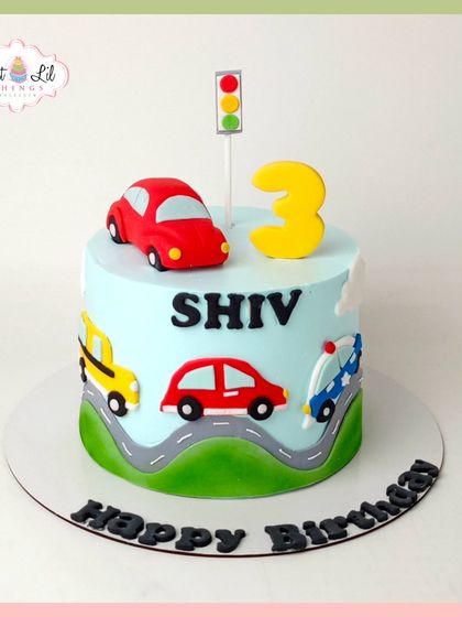 Beep beep! A cute and simple car-themed cake for a 3rd birthday. This cake features a road wrapping around it with colorful fondant cars and a traffic light on top.