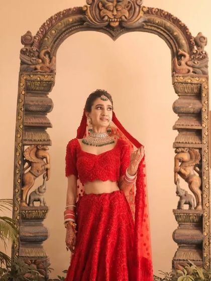 A beautiful bridal portrait in a classic red lehenga. The traditional wooden archway provides a perfect frame, blending heritage with bridal beauty.