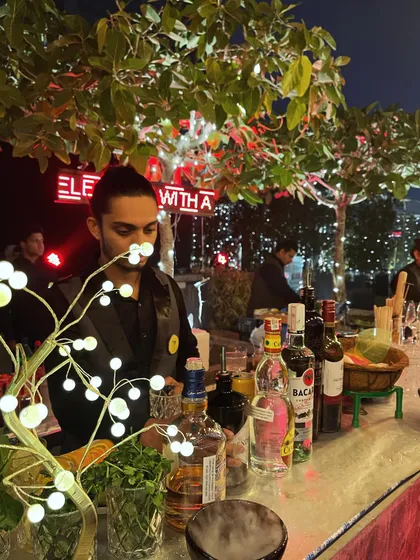 A bartender at a beautifully lit outdoor bar, surrounded by decorative trees and neon signs. This image captures the blend of professional service and stylish event design that we provide.