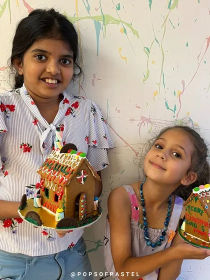 Two sisters show off their finished gingerbread houses, each one uniquely decorated with their favorite candies.