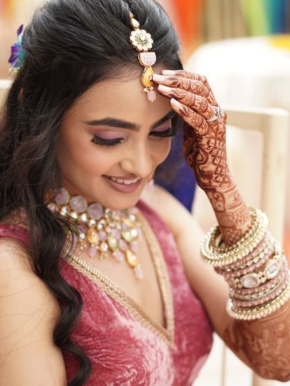 A bride's delicate pose during her Mehendi ceremony, showcasing her intricate henna design, floral jewelry, and soft makeup.