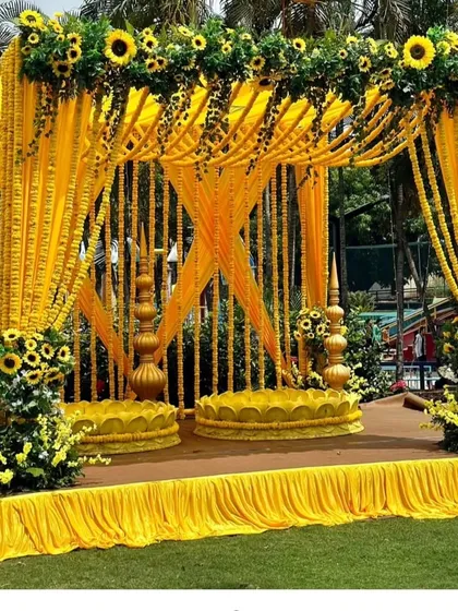 A grand outdoor Haldi mandap decorated entirely with yellow drapes and strings of marigolds and sunflowers. This creates a stunning, sun-drenched space for the ceremony.