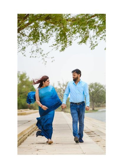 A candid shot of the couple walking by the lake. The wind catching her saree and their shared glance make it a beautiful, natural moment.