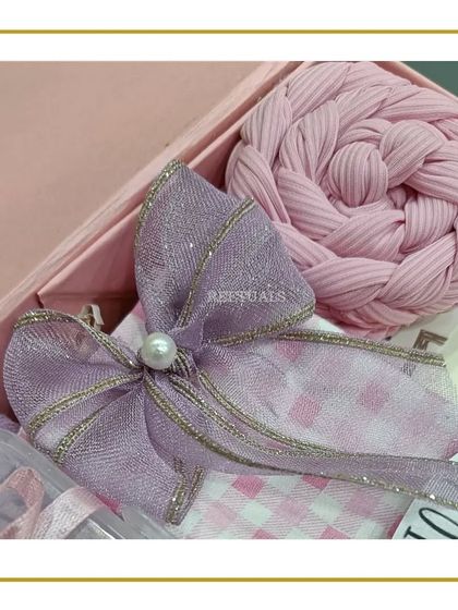 A detail shot of the gift wrapping for the baby set, featuring a lavender bow and a pink braided cloth.