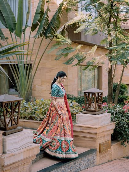 A bride descends a staircase in a garden, her colorful lehenga standing out beautifully against the natural greenery.