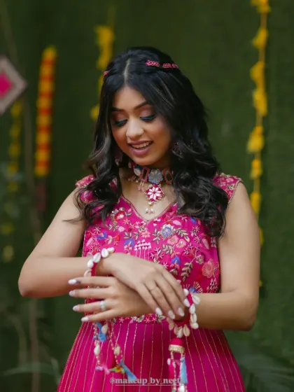 A close-up of the soft glam Haldi look. The shell jewelry and braided hairstyle add a trendy, bohemian vibe to her pink outfit.