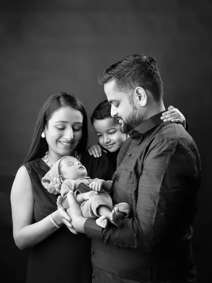 A tender black and white photo of the family gazing lovingly at their sleeping newborn.