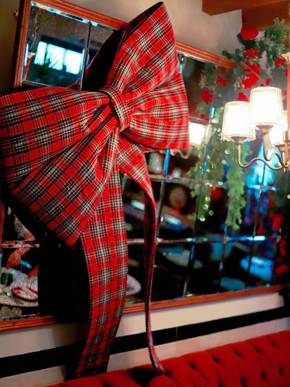 A mirror adorned with an oversized tartan bow, reflecting the warm, festive lights of the room.