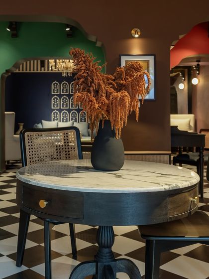 A round dining or center table with a marble top and a dark, turned-wood pedestal base. This piece, from our House of Goya collection, is paired with a cane-back chair, showcasing our mix-and-match philosophy.