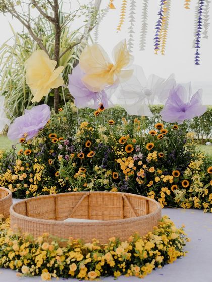 A close-up of the Haldi ceremony area, showing the wicker baskets nestled in a bed of sunflowers and the large, translucent butterfly bows that add a touch of magic.