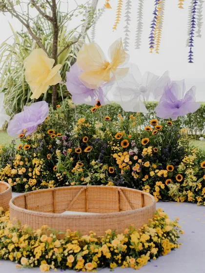 A close-up of the Haldi ceremony area, showing the wicker baskets nestled in a bed of sunflowers and the large, translucent butterfly bows that add a touch of magic.
