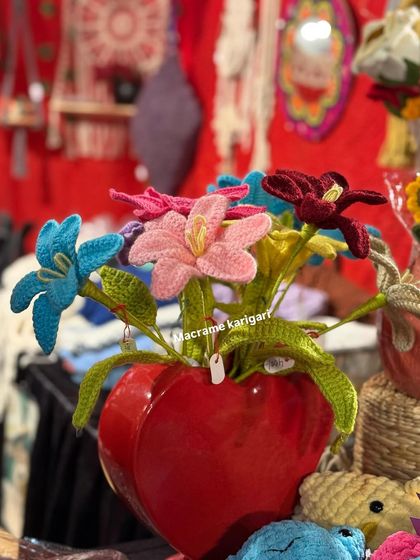 A bouquet of our colorful open-petal crochet flowers in a heart-shaped red vase, seen at one of our exhibition stalls.