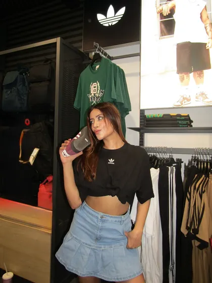 An in-store shot at Adidas, styling a black crop top with a pleated denim mini skirt.