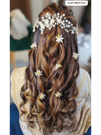 A hairstyle can complete the entire bridal look. These soft curls, adorned with delicate floral and pearl accessories, create a romantic and glamorous feel. This style is perfect for a Nikah, reception, or sangeet event.