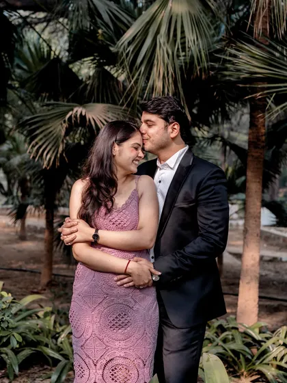 A tender forehead kiss surrounded by lush palm trees. The natural greenery provides a beautiful, intimate backdrop for this romantic gesture.