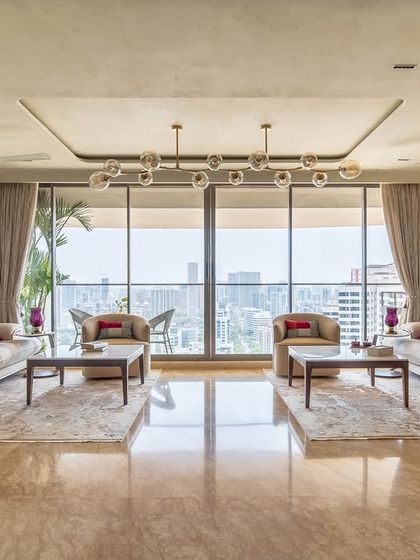 The 'Eternity' living room, showcasing a grand seating arrangement with panoramic city views. The design uses a neutral base with pops of red and traditional Indian art for a culturally rich yet modern feel.