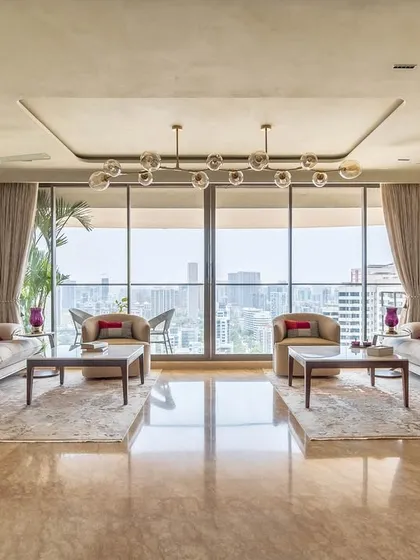 The 'Eternity' living room, showcasing a grand seating arrangement with panoramic city views. The design uses a neutral base with pops of red and traditional Indian art for a culturally rich yet modern feel.