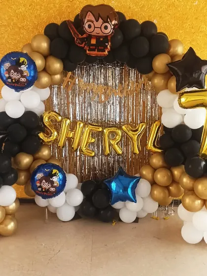 A magical Harry Potter themed balloon decoration. Using the house colors of black and gold, this setup includes a foil curtain backdrop and character foil balloons for a 7th birthday celebration at Hogwarts.
