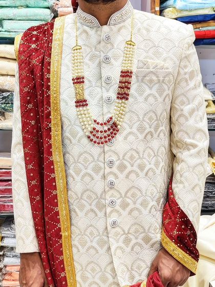 A close-up of an ivory sherwani with detailed hand embroidery, paired with a red and pearl necklace. This combination is perfect for a traditional wedding ceremony.