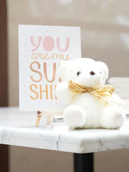 A tiny white teddy bear with a gold bow sits next to a sweet "You are my Sunshine" card. This simple, adorable detail adds so much warmth to the decor.