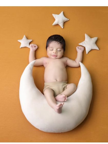 A happy dreamer on a crescent moon. This portrait against a warm mustard background captures a sweet, sleepy smile, making for a truly heartwarming image.
