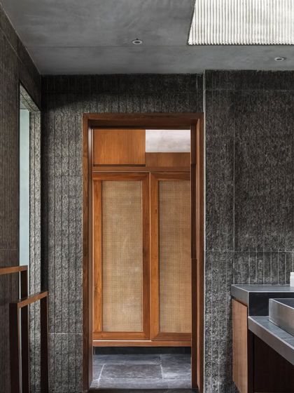 The bathroom in the Brick House is a sanctuary of texture, with rough-hewn stone walls, smooth wooden cabinetry, and a skylight that washes the space in soft, diffused light.