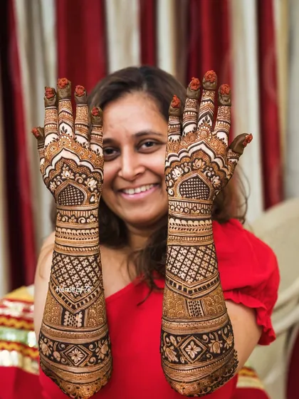 A happy bride showcasing her full, traditional bridal mehendi. The design is dense with geometric patterns and classic motifs.