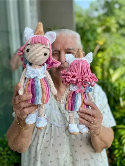 Dadi holding our magical Bella unicorn dolls. These dolls feature rainbow dresses, unicorn horns, and beautiful curly pink hair.