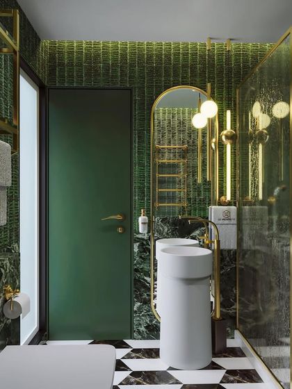 A bathroom that blends gold elements, sleek marble, and a black-and-white checkered floor. The gold fixtures and pedestal sinks add a touch of vintage glamour.