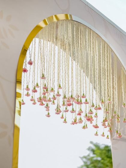 A detailed view of the hanging floral chandelier within the entrance arch. Delicate pink flower buds hang from strings of jasmine, creating a beautiful and fragrant welcome for guests.