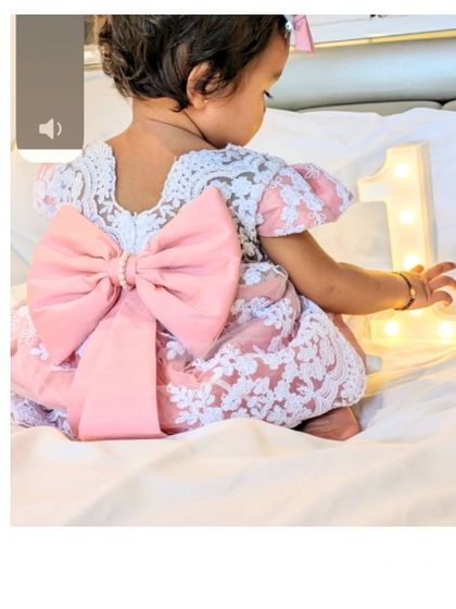 The "Arya" dress is all about that bow. This back view shows the oversized pink satin bow that makes this white lace dress a true statement piece for any first birthday party.