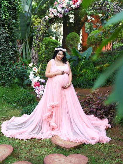 A beautiful solo portrait of a mom-to-be in a pink gown, standing in a garden with a rustic floral arch.