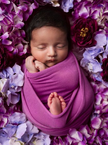 A truly stunning portrait of a newborn nestled in a bed of vibrant purple flowers. This is a perfect example of a highly creative and artistic setup.