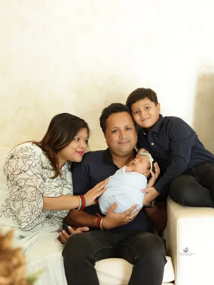 A beautiful family portrait welcoming a newborn. The parents and their older son are gathered on a couch, all focused on the tiny new baby, capturing a moment of quiet family connection.