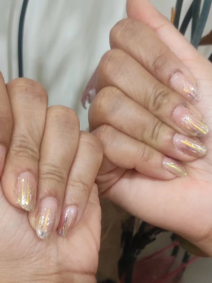 Sheer nail extensions with scattered gold foil flakes, creating a look of gold leaf suspended in the nail.