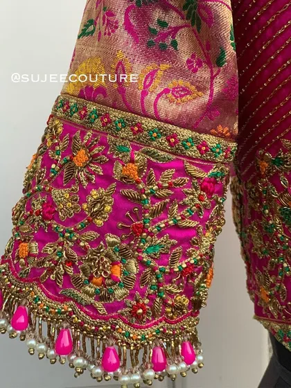 A close-up of the sleeve cuff on the pink brocade blouse. This view highlights the dense, multi-colored floral embroidery and the beautiful pink and pearl bead tassels.