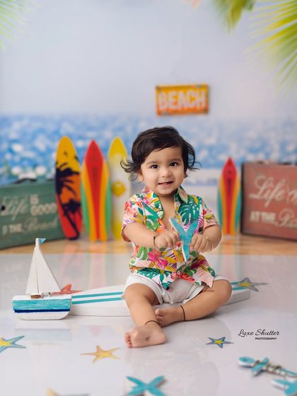 A cute baby boy enjoying our fun, summery beach-themed setup, complete with a surfboard prop and ocean backdrop.