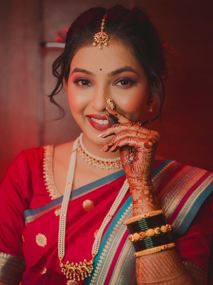 A shy, beautiful smile from the bride as she adjusts her nath. This close-up portrait captures her coy expression and the intricate details of her Maharashtrian bridal look.