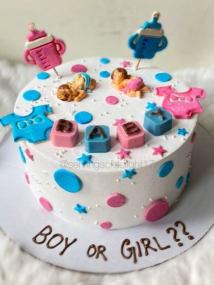 A "Boy or Girl?" gender reveal cake decorated with cute, handcrafted fondant baby clothes, bottles, and sleeping babies.