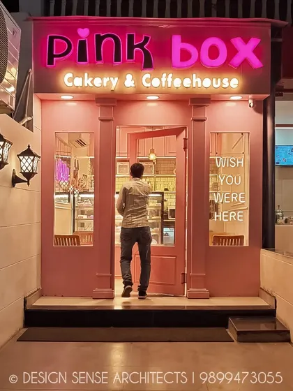 The entrance acts as a perfect frame for the sweet world inside. This view shows a customer stepping into the bakery, drawn in by the glowing pink facade.